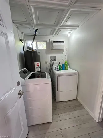 Clothes washing area with electric water heater, a wall unit AC, light wood-type flooring, and independent washer and dryer