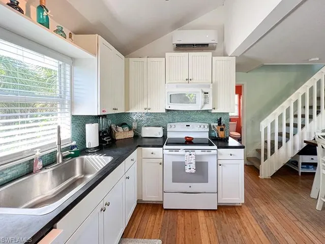 Kitchen featuring white appliances, sink, light hardwood / wood-style flooring, lofted ceiling, and backsplash