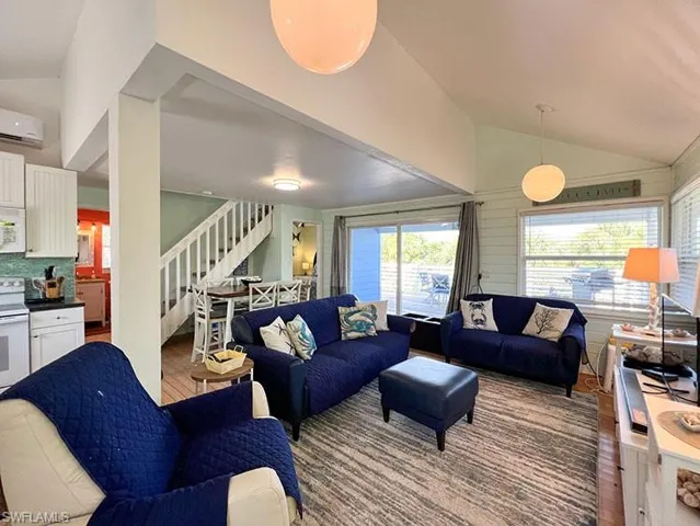 Living room with wood-type flooring, an AC wall unit, and high vaulted ceiling