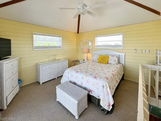 Bedroom with wood walls, carpet floors, ceiling fan, and vaulted ceiling