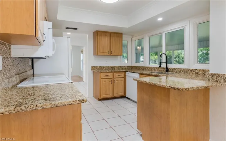 Kitchen with tasteful backsplash, a peninsula, light stone counters, white appliances, and light tile patterned flooring