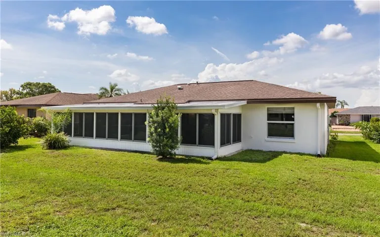Back of house featuring a sunroom, a yard, roof with shingles, and stucco siding