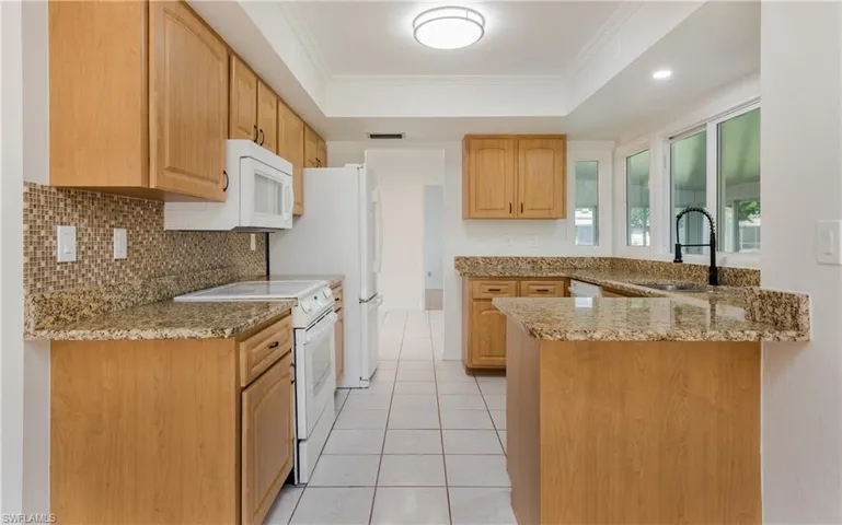 Kitchen with white appliances, a peninsula, light stone countertops, decorative backsplash, and a raised ceiling