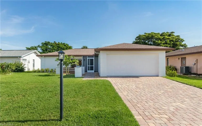 Ranch-style house featuring decorative driveway, a front lawn, an attached garage, and stucco siding