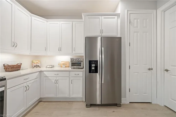 Kitchen featuring stainless steel fridge with ice dispenser, white cabinetry, decorative backsplash, light stone counters, and wood tiled floors