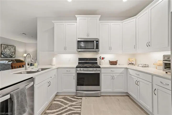 Kitchen featuring appliances with stainless steel finishes, white cabinets, tasteful backsplash, light stone counters, and open floor plan