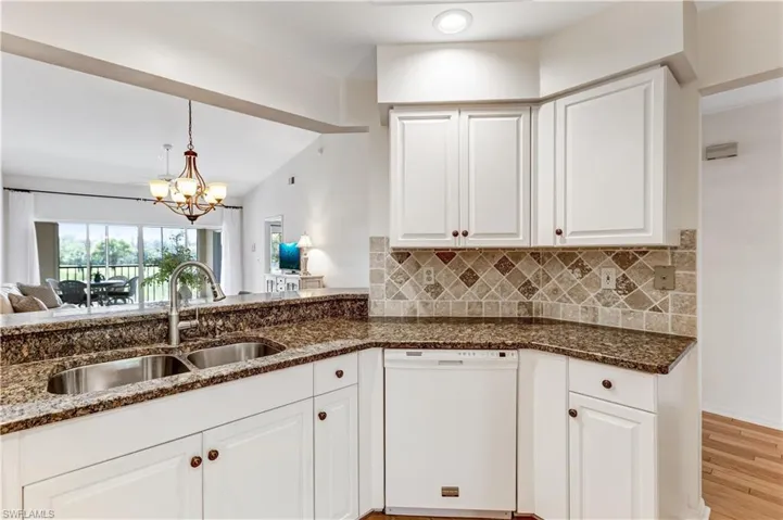 Kitchen with white cabinetry, white dishwasher, lofted ceiling, dark stone counters, and a chandelier