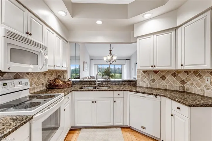 Kitchen featuring white appliances, white cabinets, suspended lighting, and dark stone countertops