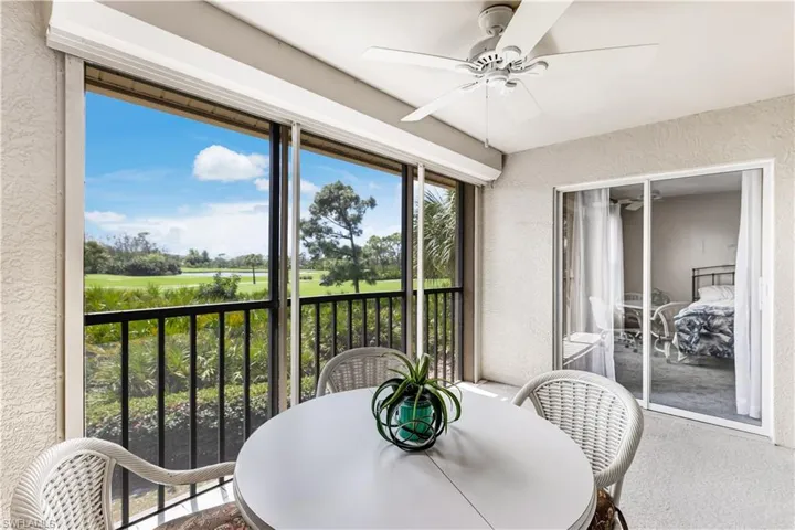 Sunroom with view of golf course, a balcony, ceiling fan, and outdoor dining area