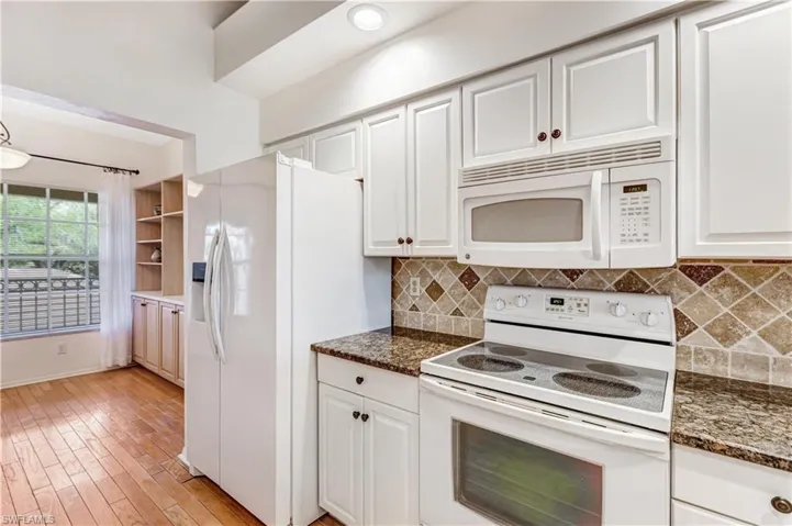 Kitchen with white appliances, white cabinets, light wood-style flooring, and dark stone counters
