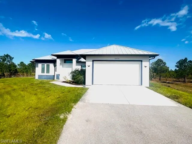 View of front of house featuring concrete driveway, a front lawn, an attached garage, stucco siding, and a standing seam roof