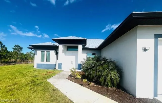 Entrance to property featuring a lawn, stucco siding, a standing seam roof, and a metal roof