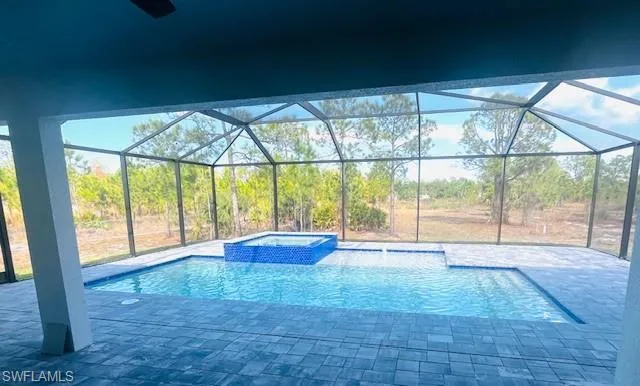 View of pool with a sunroom, a pool with connected hot tub, a patio, and glass enclosure