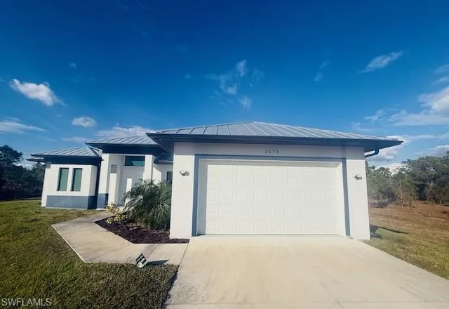 View of front of house featuring driveway, a front lawn, a standing seam roof, a metal roof, and stucco siding