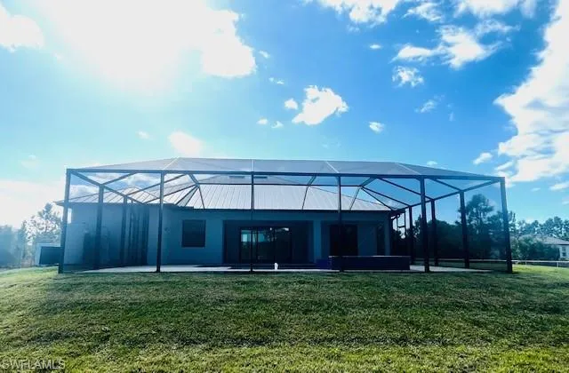 Rear view of house with glass enclosure, a lawn, and a sunroom