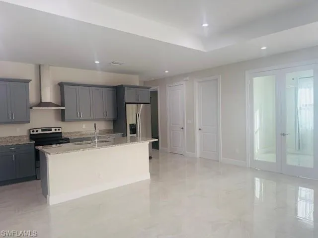 Kitchen featuring french doors, appliances with stainless steel finishes, gray cabinets, light stone countertops, and wall chimney range hood