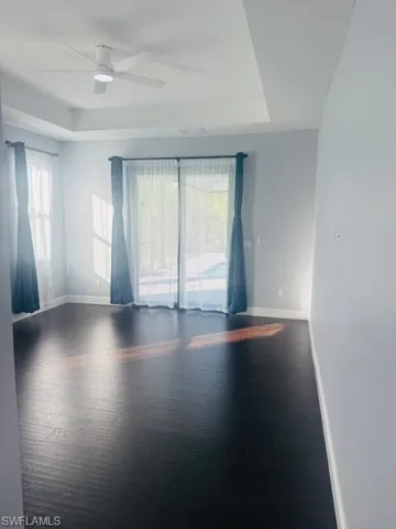 Unfurnished room with dark wood-type flooring, a tray ceiling, plenty of natural light, and ceiling fan