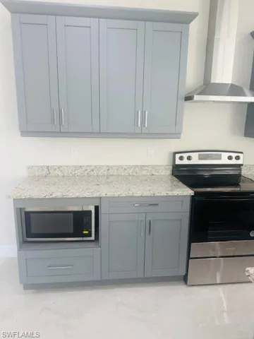 Kitchen featuring appliances with stainless steel finishes, wall chimney exhaust hood, light stone counters, and gray cabinets