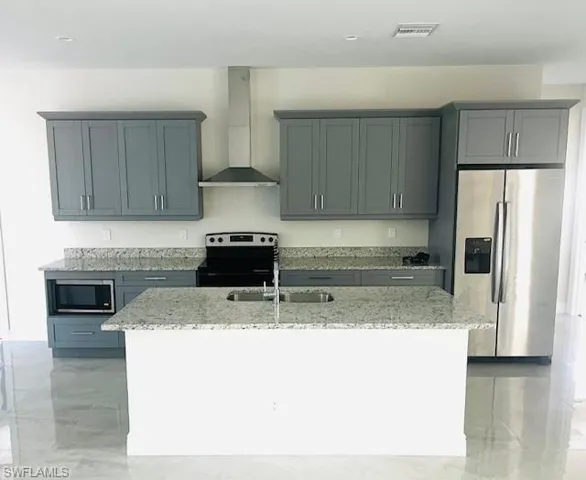 Kitchen with light stone counters, appliances with stainless steel finishes, wall chimney range hood, and gray cabinetry