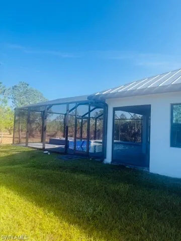 View of grassy yard featuring glass enclosure and a sunroom