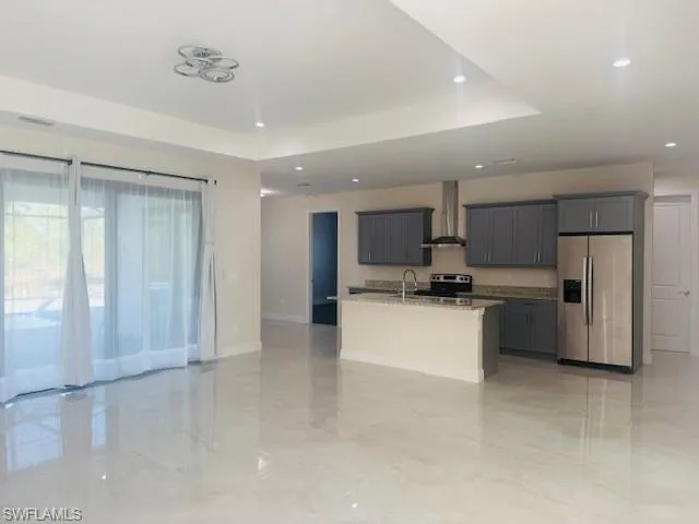 Kitchen with open floor plan, stainless steel appliances, a kitchen island with sink, wall chimney range hood, and gray cabinetry