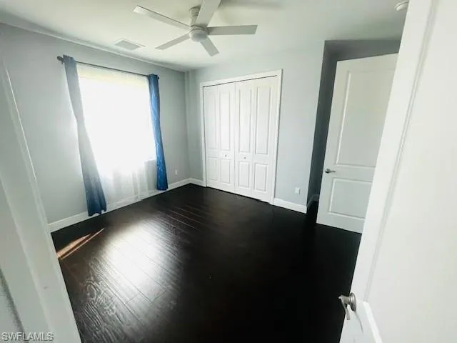 Unfurnished bedroom with dark wood-style floors, a ceiling fan, and a closet