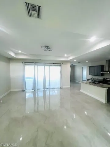 Unfurnished living room featuring light marble finish floors, a raised ceiling, and recessed lighting