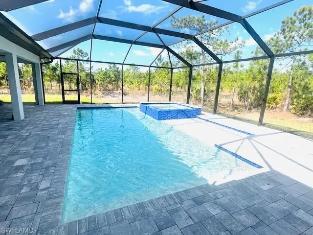 View of swimming pool featuring a sunroom, a pool with connected hot tub, glass enclosure, and a patio area