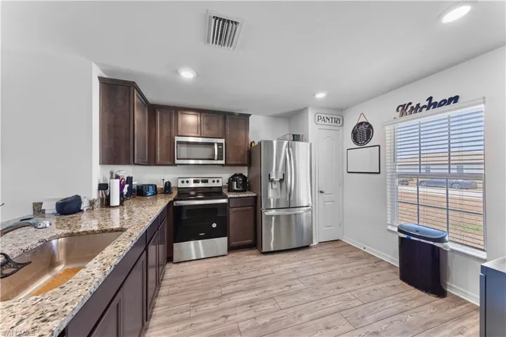 Kitchen featuring visible vents, dark brown cabinetry, a sink, light wood-style flooring, and stainless steel appliances