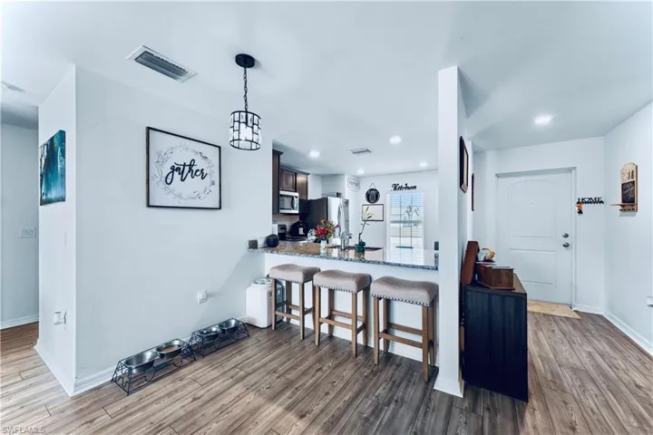 Kitchen with appliances with stainless steel finishes, a breakfast bar, baseboards, wood finished floors, and visible vents