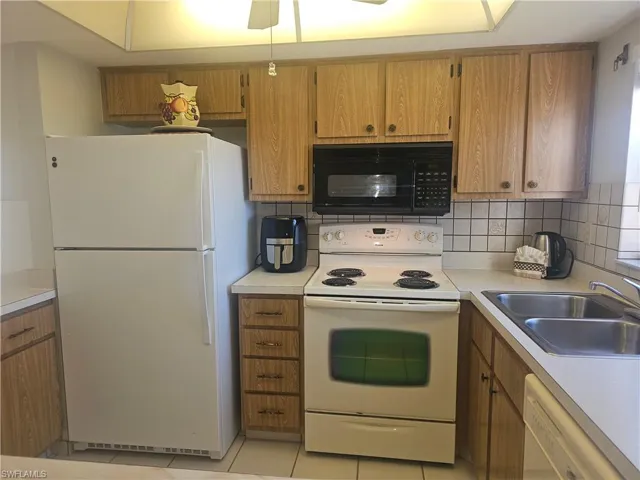 Kitchen featuring white appliances, light countertops, wood finish cabinetry, tasteful backsplash, and light tile patterned floors