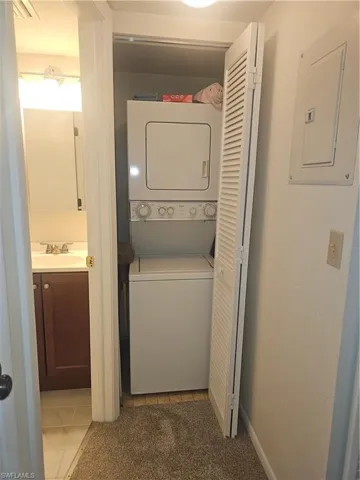 Laundry area featuring stacked washer / dryer, electric panel, carpet floors, and tile patterned flooring