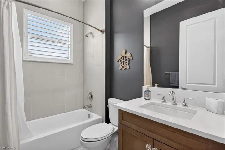 Bathroom featuring a white bathtub, light-toned wall tiling, a window with horizontal blinds, a dark accent wall, and a vanity with a white countertop and a built-in sink