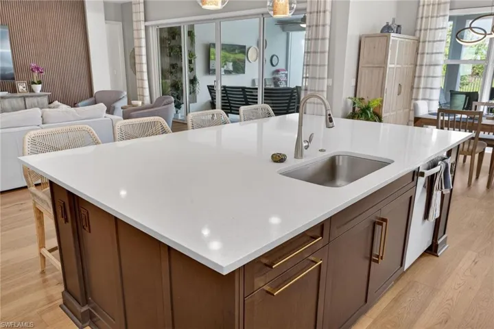 Kitchen island with a white countertop and integrated sink, featuring dark wood cabinetry with gold-tone hardware