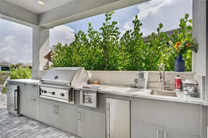 Outdoor kitchen featuring a built-in stainless steel grill, integrated sink with faucet, under-counter refrigeration, and stone countertops