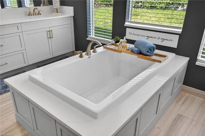 Built-in soaking tub with a light gray panel surround and a white stone-finish deck
