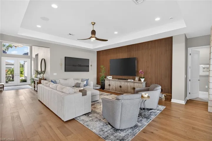 Open-concept living area featuring wood-finish flooring, a tray ceiling with recessed lighting, and a modern ceiling fan