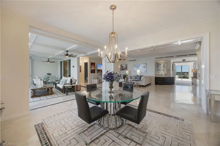 Dining space with a chandelier, a ceiling fan, coffered ceiling, crown molding, and beamed ceiling