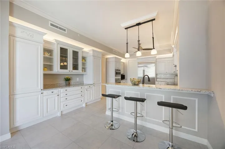 Kitchen with a breakfast bar area, open shelves, light stone countertops, glass insert cabinets, and ornamental molding