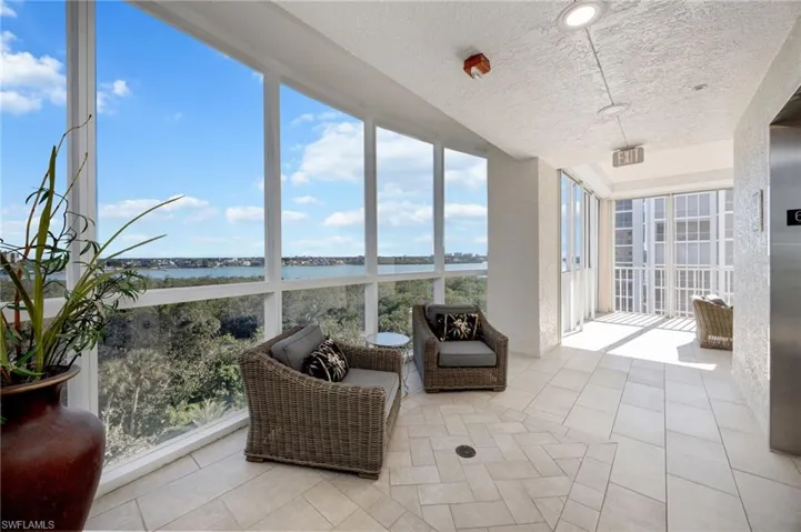 Sunroom with expansive windows, tile patterned flooring, a water view, elevator, and a textured ceiling