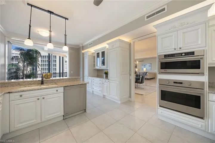 Kitchen featuring stainless steel appliances, light stone countertops, hanging light fixtures, white cabinets, and ornamental molding