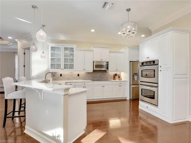 Kitchen with decorative light fixtures, white cabinetry, decorative backsplash, and stainless steel appliances