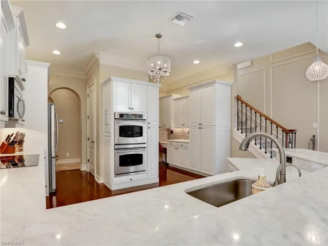 Kitchen with stainless steel appliances, light stone counters, hanging light fixtures, and sink