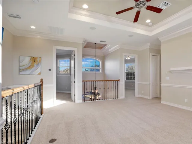 Hall with a tray ceiling, ornamental molding, light carpet, and a notable chandelier