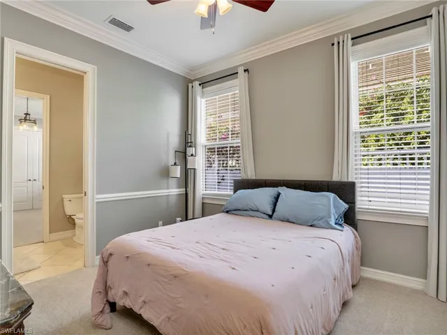Carpeted bedroom with ceiling fan, crown molding, and ensuite bath
