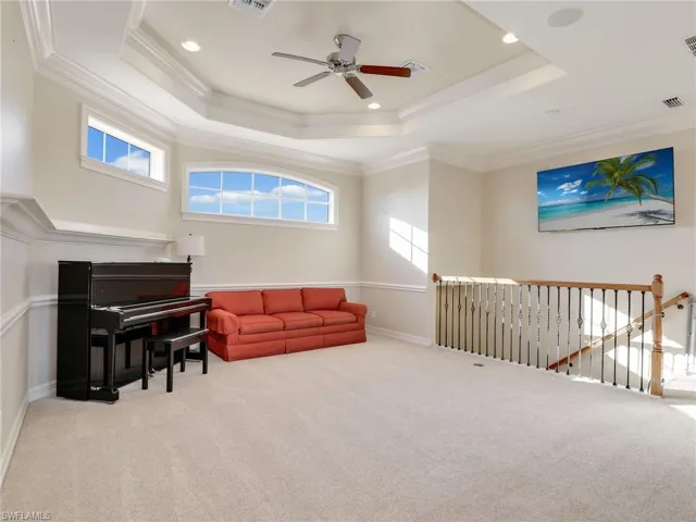 Living area featuring ceiling fan, light carpet, ornamental molding, and a raised ceiling