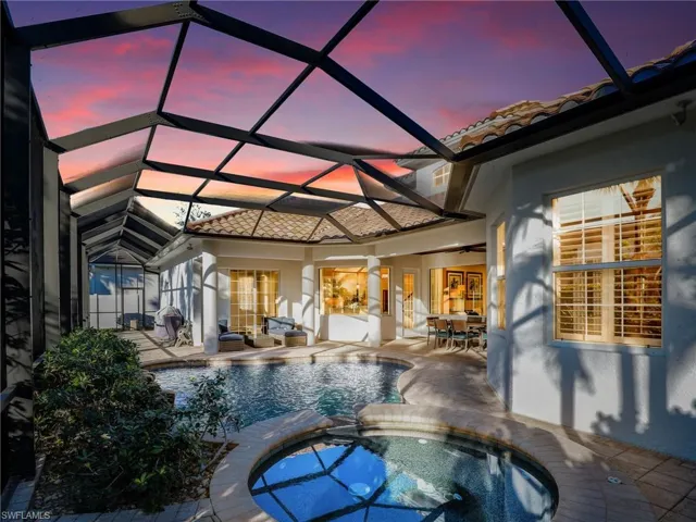 Pool at dusk with a patio area, a grill, glass enclosure, and an in ground hot tub