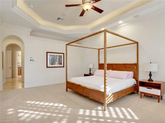 Carpeted bedroom featuring ceiling fan, ornamental molding, and a tray ceiling