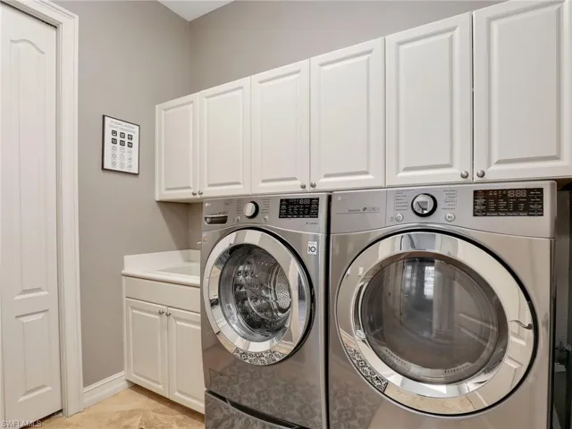 Laundry area with cabinets, light tile patterned floors, separate washer and dryer, and sink
