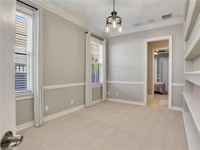 Carpeted empty room featuring ceiling fan with notable chandelier and ornamental molding